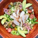 Loaded Italian Chopped Salad with chicken, chickpeas, salami, and avocado arranged in a large wooden salad bowl.