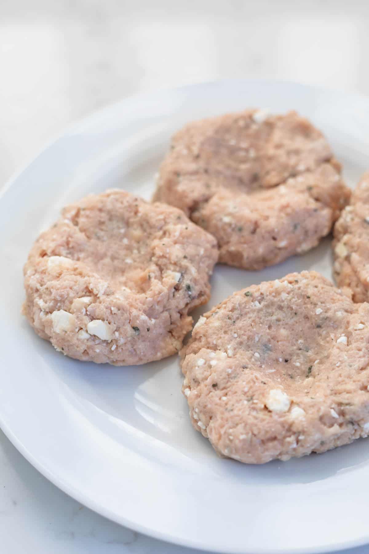 four raw chicken patties formed on a white plate