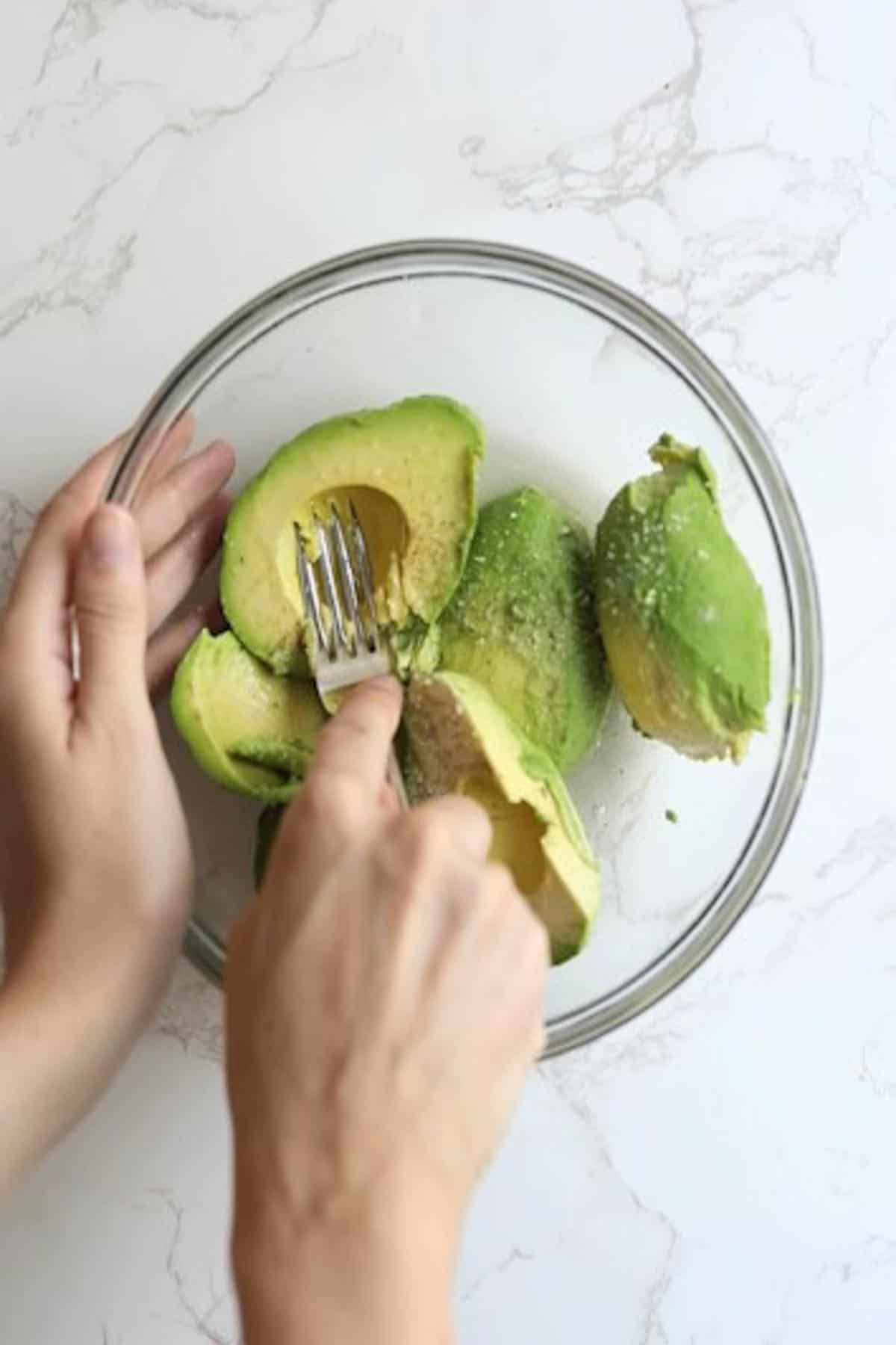 avocados in a glass bowl being smashed with a fork