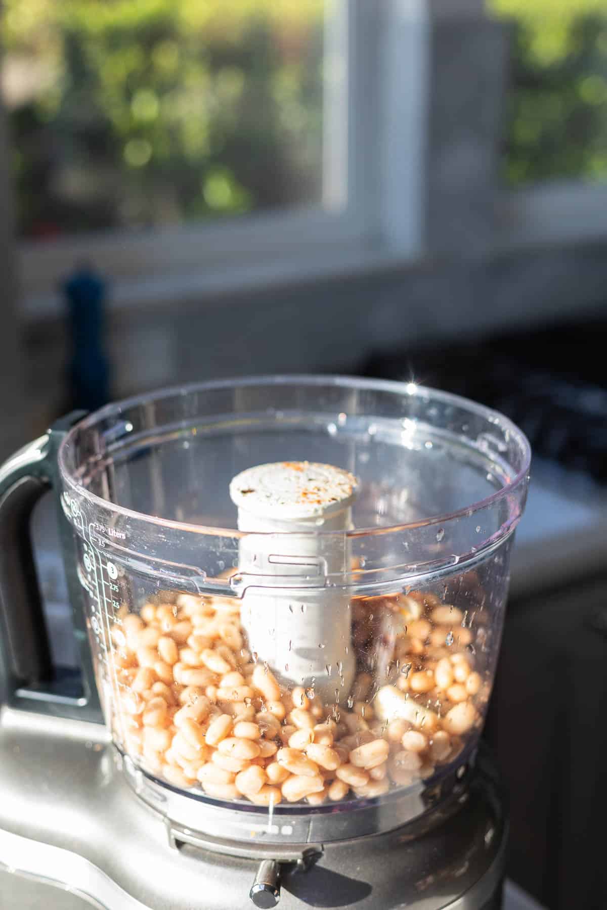silver food processor without a lid and with white beans inside
