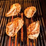 Four easy marinated chicken breasts on a grill under flame.