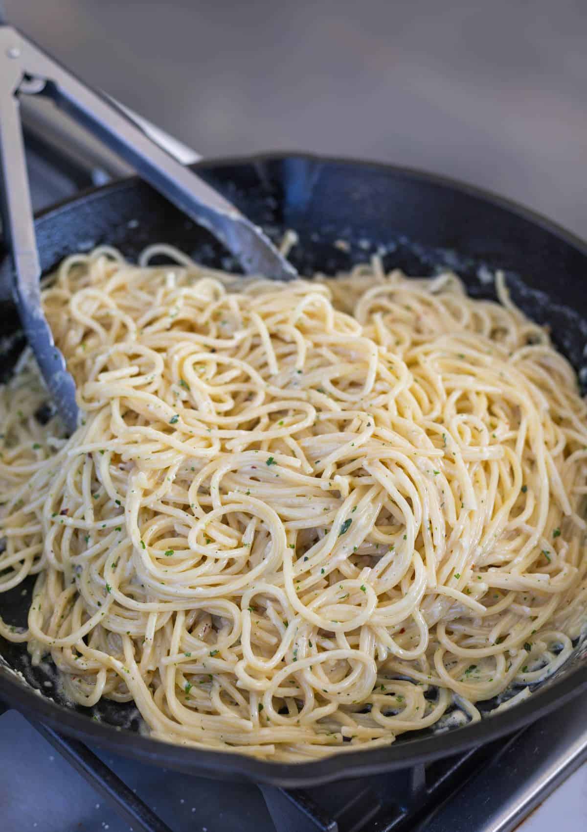 creamy spaghetti being tossed in a cast iron skillet with tongs