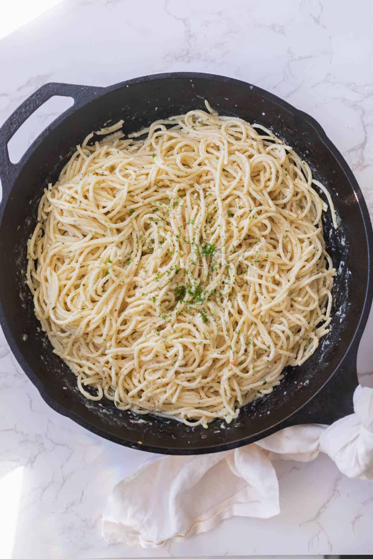creamy lemon garlic pasta in a black cast iron pan with a white napkin