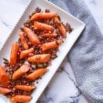 Roasted carrots tossed with crispy pancetta and pumpkin seeds on a white platter.