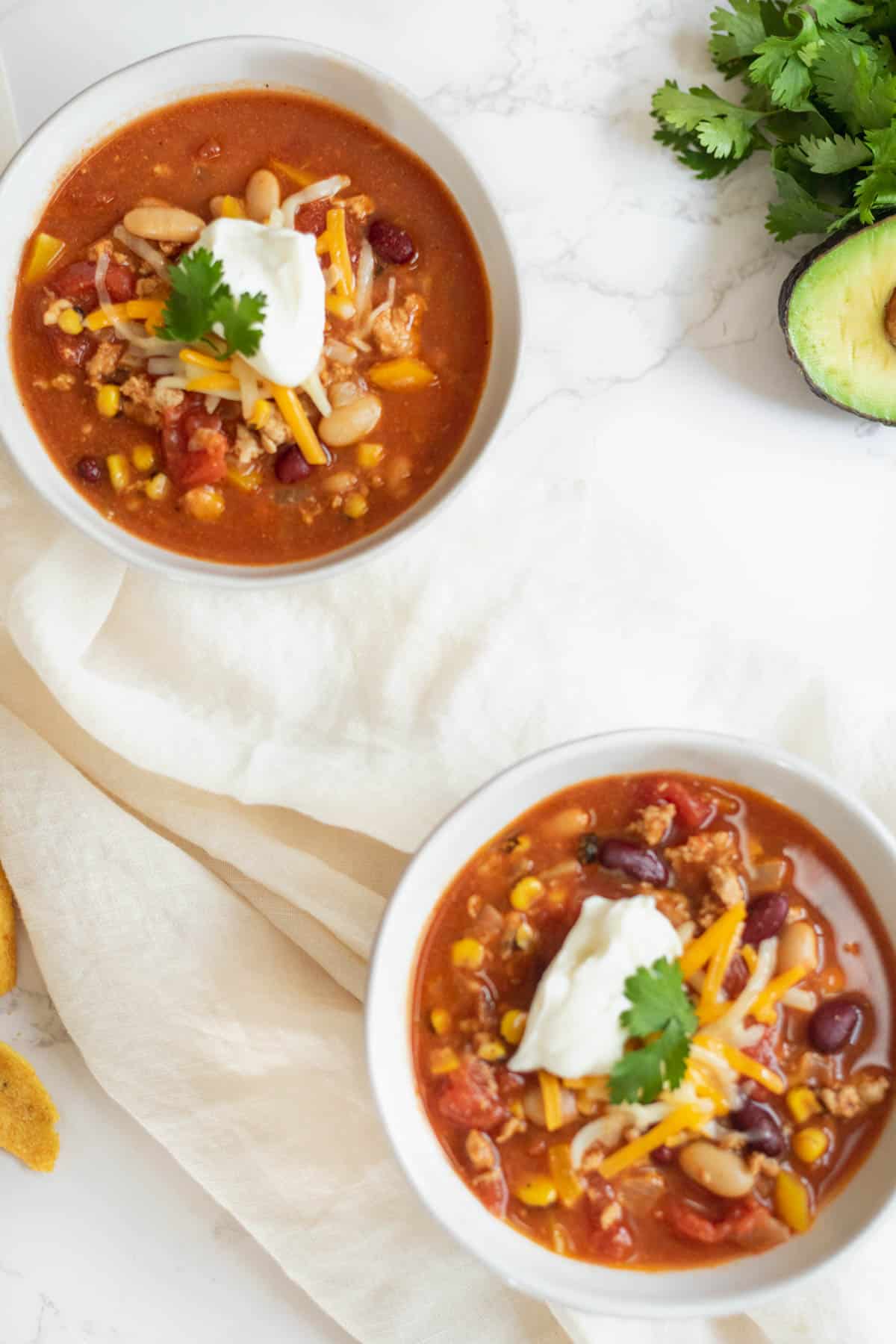 overhead photo of two bowls of turky chili with sour cream on them on a white towel