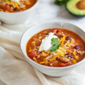 turkey chili in a white bowl next to half an avocado and a second bowl on a white counter