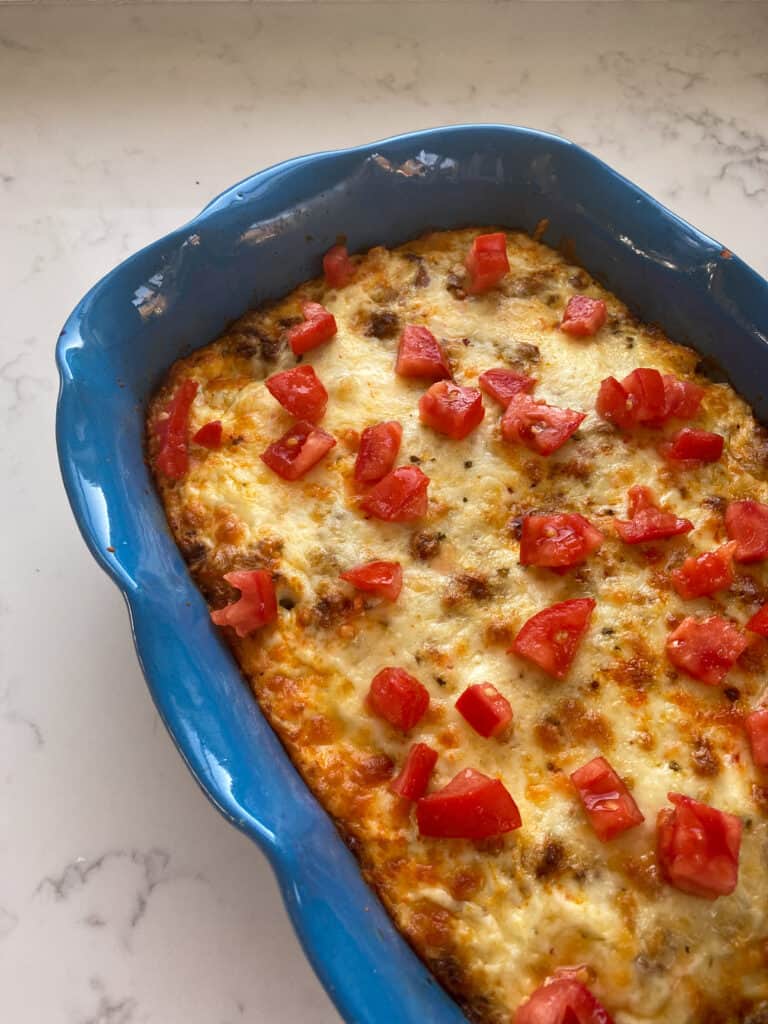a blue casserole dish of the breakfast casserole topped with tomatoes
