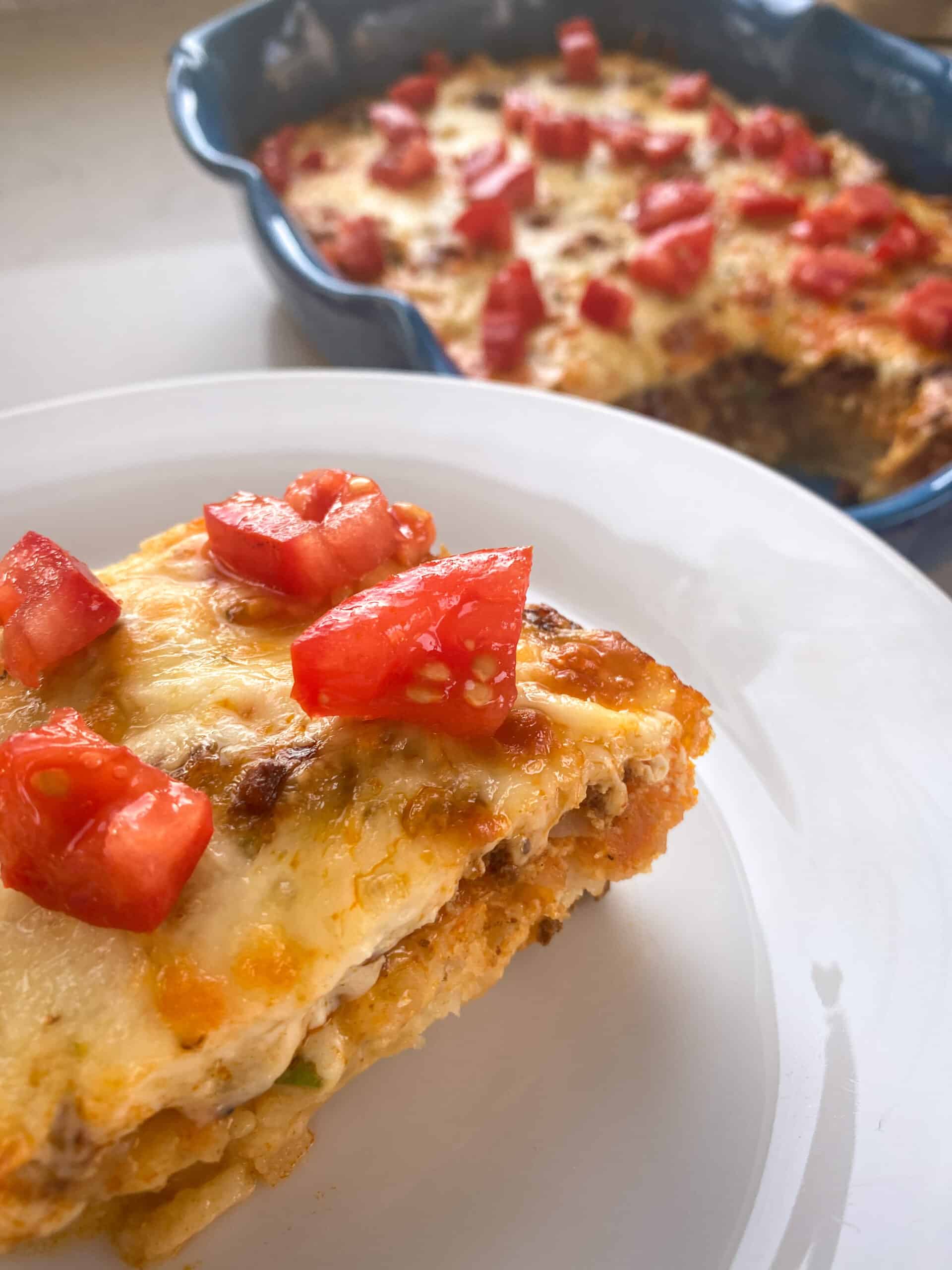 blue casserole dish with breakfast casserole and a white plate with a slice of the casserole topped with tomatoes