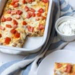 Chorizo Egg Bake in a casserole dish next to a bowl of sour cream, plate, and blue and white towel.