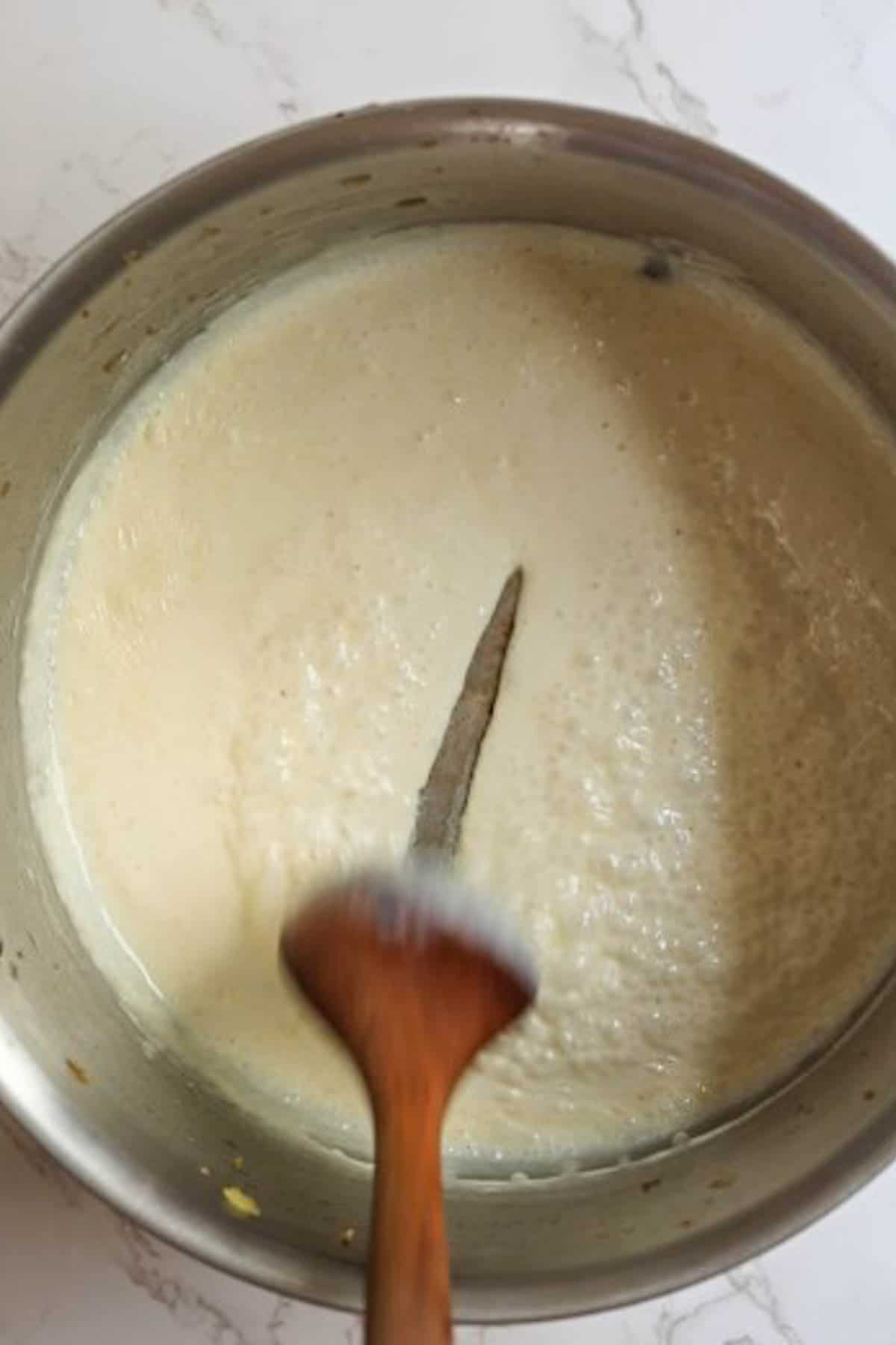 heavy cream reducing in a large silver pot with a wooden spoon