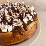 Chocolate peanut butter cheesecake with a chocolate cookie crust topped with popcorn and drizzled with chocolate genache on a white plate.