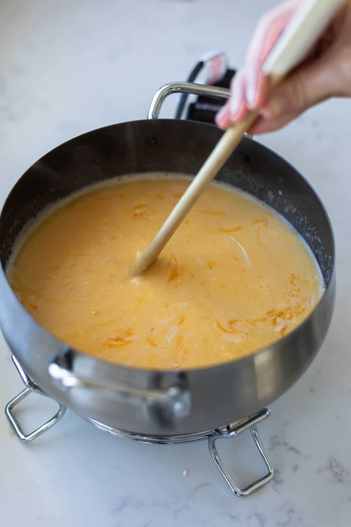 cheese fondue being stirred with a wooden spoon