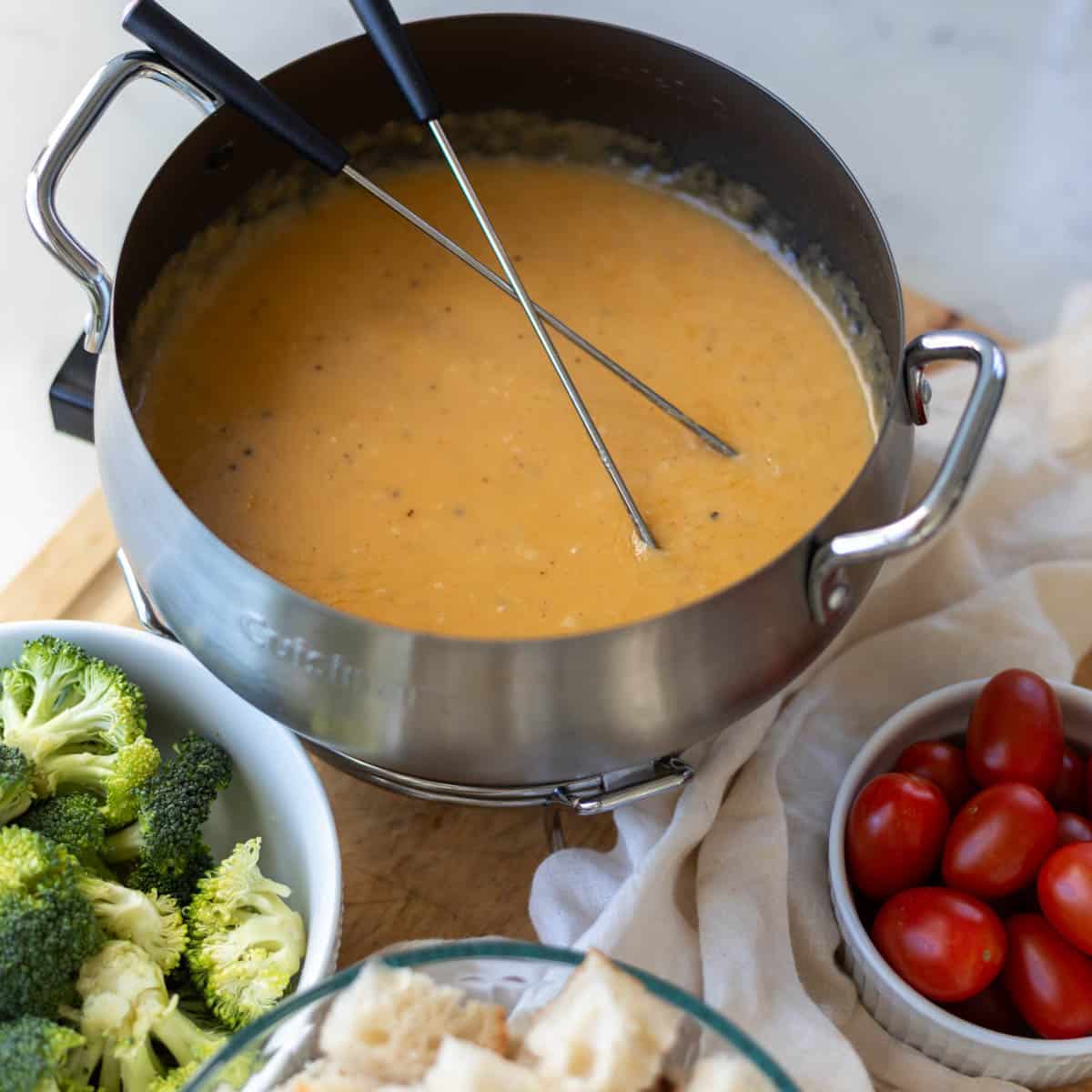 cheese fondue in a bot with skewers next to broccoli, bread, and tomatoes