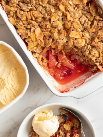 strawberry crisp in a baking dish next to a tub of vanilla ice cream and a bowl of crisp topped with a scoop of ice cream
