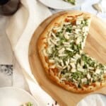 Savory Apple Pizza with Broccoli and Cheese on a wooden pizza board next to a glass of wine.