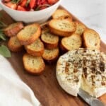 Grilled brie on a wooden board with crostini, fresh strawberries, and basil.