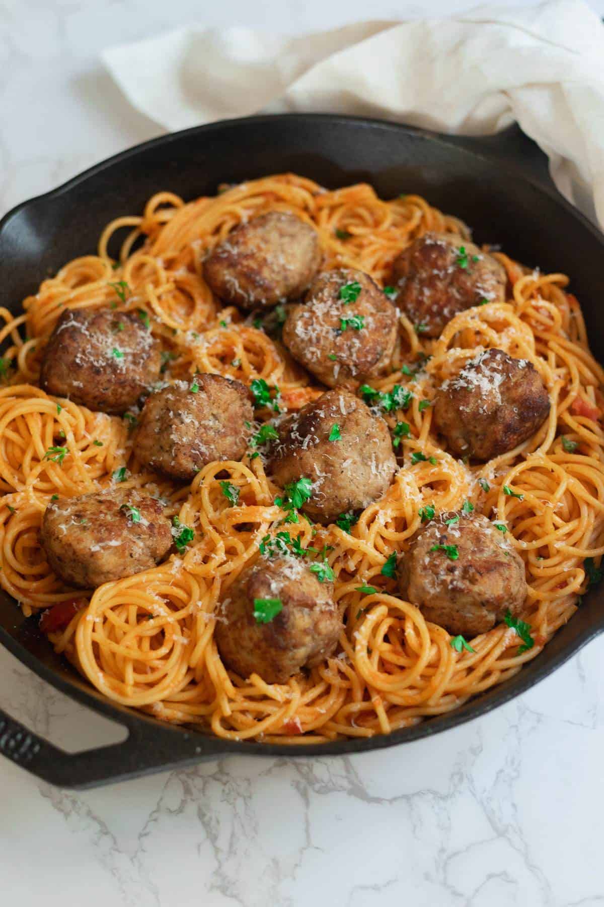 meatballs surrounded by spaghetti in tomato sauce in a cast iron skillet