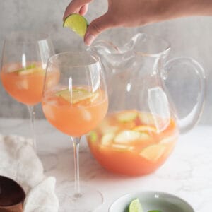 lime being squeezed into a wine glass of sangria with a pitcher