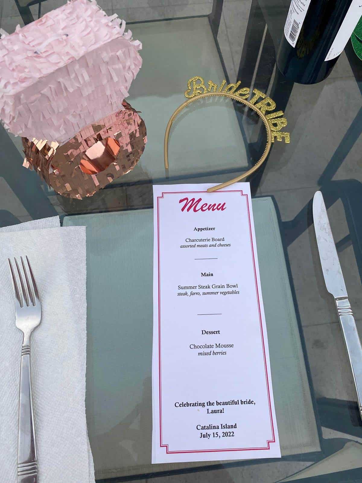 table setting on a glass table with menu, pink ring, and gold crown