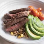 Skirt steak grain bowl with farro, cherry tomatoes, avocado, and corn in a white bowl.