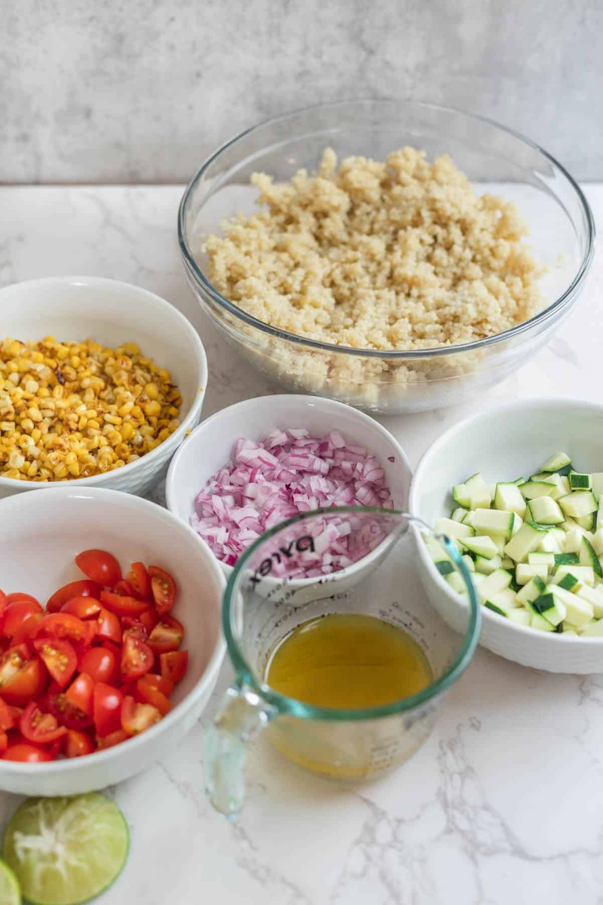 bowls of ingredients including quinoa, corn, shallots, zucchini, tomatoes, limes, and olive oil