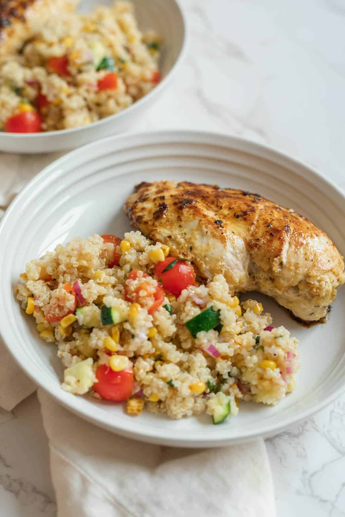 two white plates of summer quinoa salad with a grilled chicken breast
