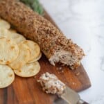 Pecan Goat Cheese Log on a wooden board next to crackers, a knife, and fresh rosemary.