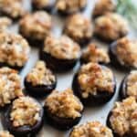 Platter of sausage and cream cheese stuffed mushrooms with a thyme sprig in the back.
