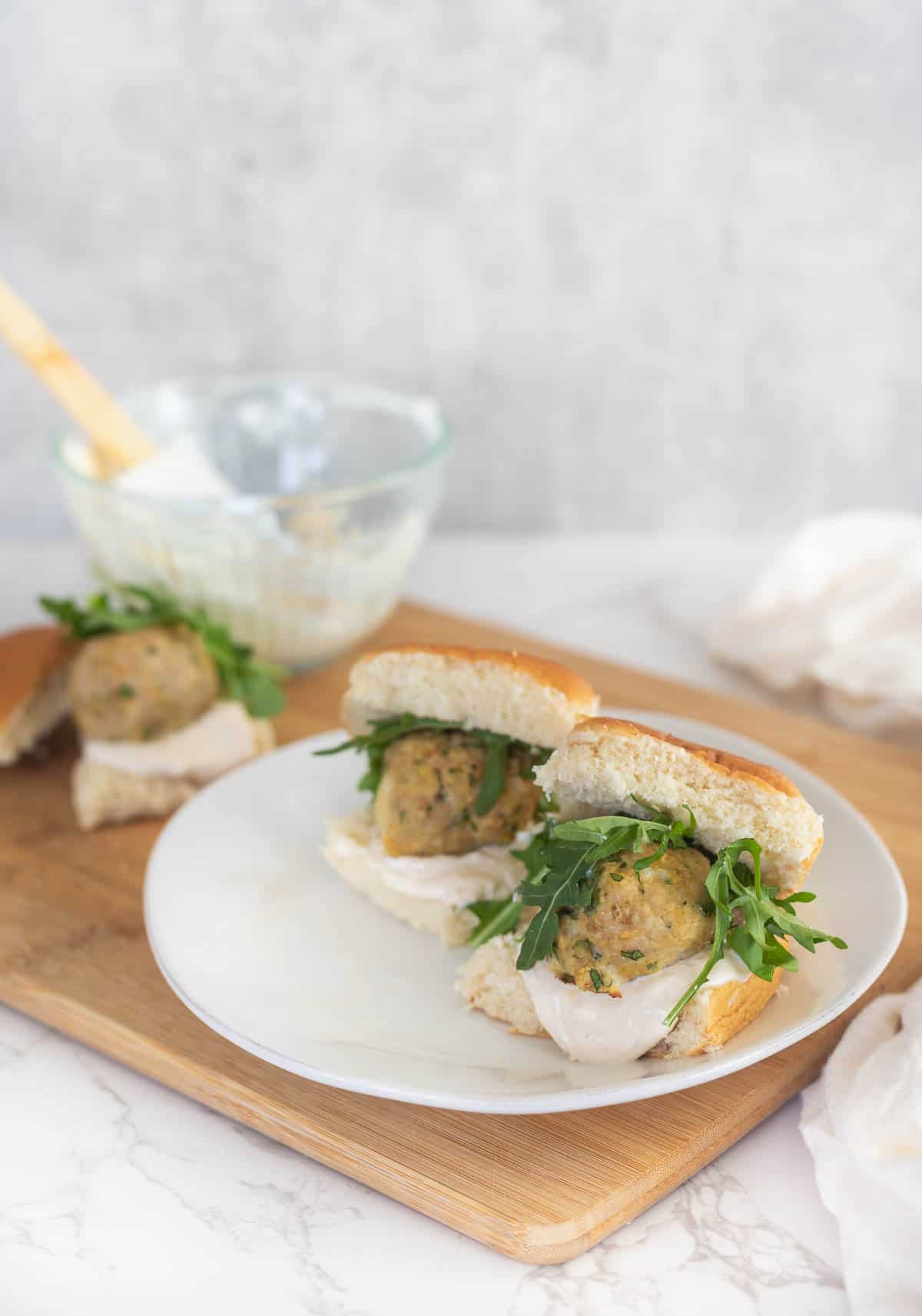 two chicken meatball slilders on a plate on a wooden cutting board with yogurt sauce in a clear bowl