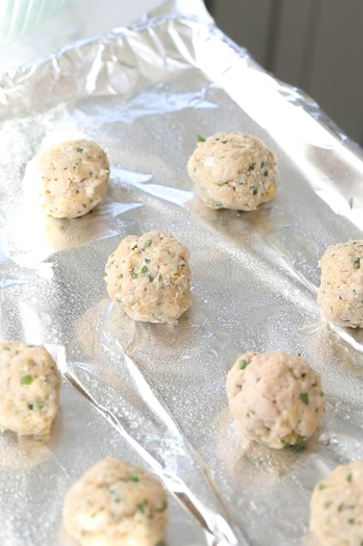 Raw chicken meatballs rolled into balls on foil.