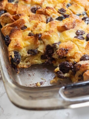 chocolate and cherry bread pudding in a clear rectangular dish with a serving missing