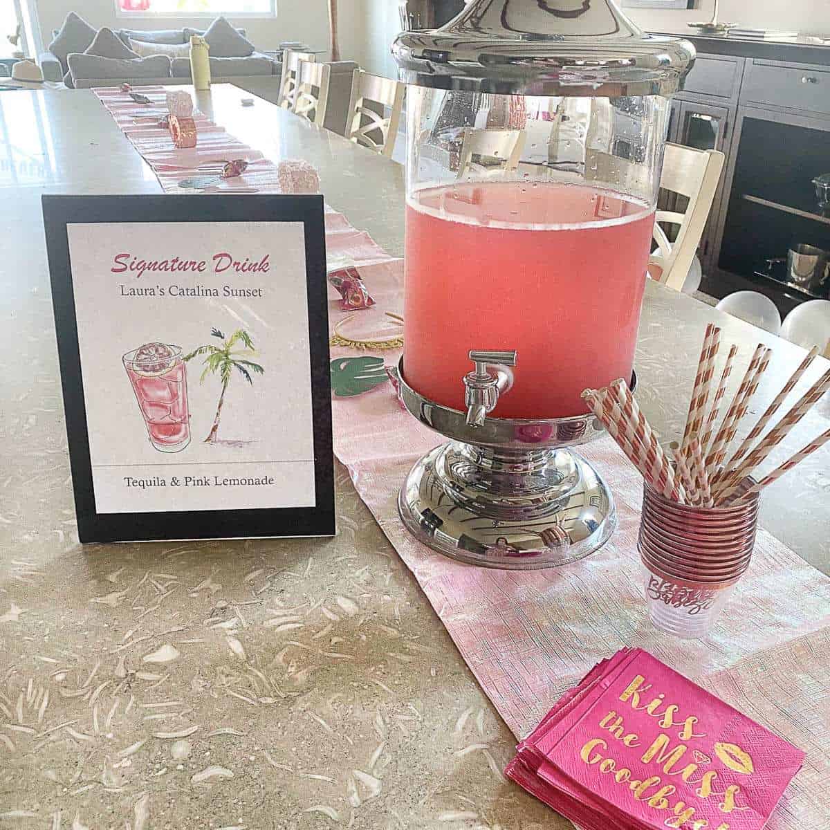 Pink lemonade in a large pitcher with straws and a signature drink sign