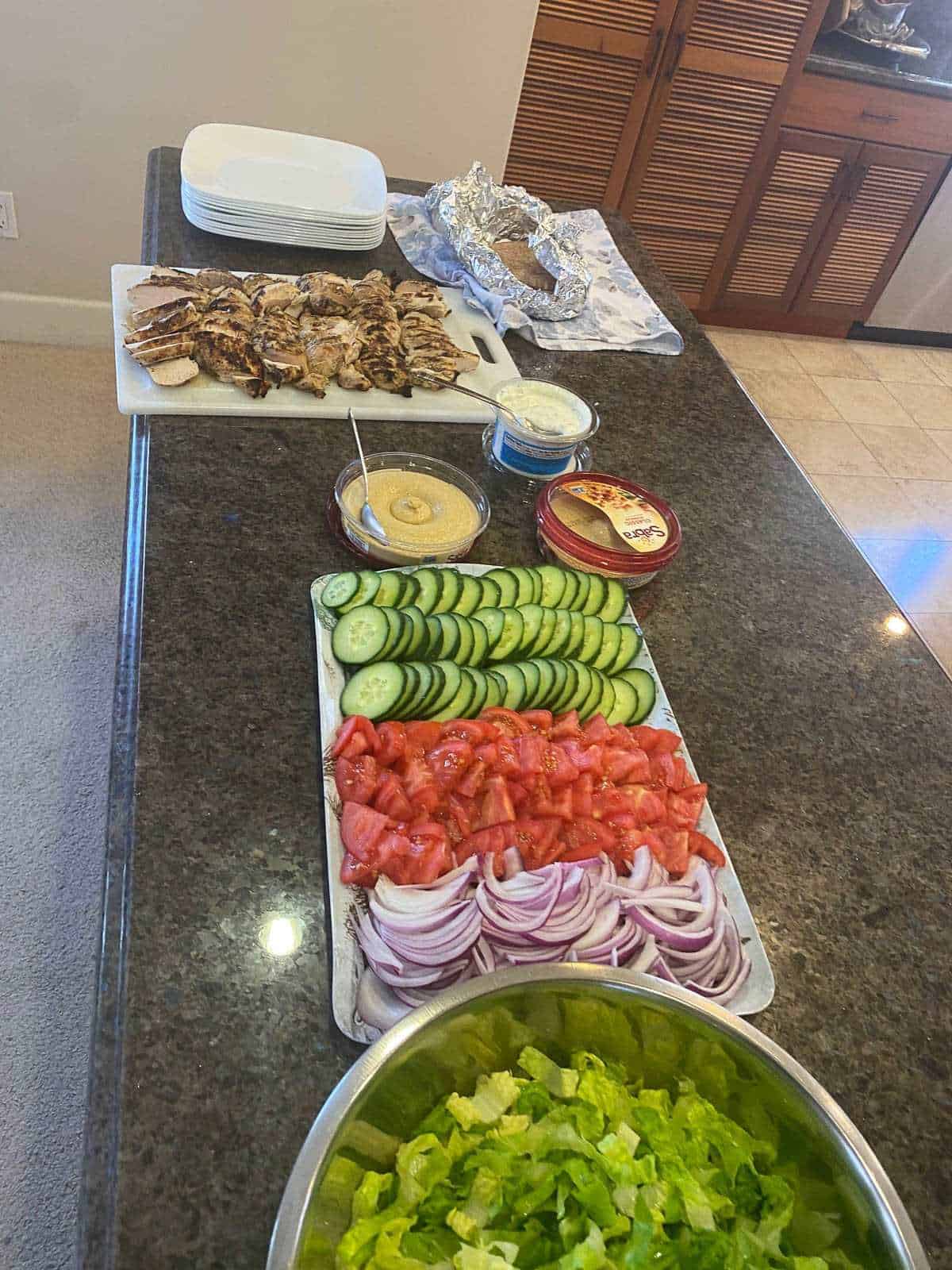 grilled chicken, hummus, and vegetables lined up on a black counter