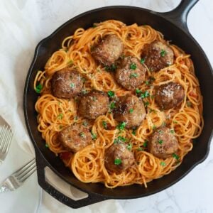 meatballs in a cast iron skillet surrounded by spaghetti in tomato sauce