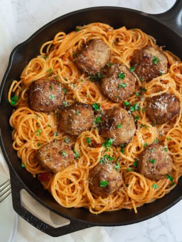 meatballs in a cast iron skillet surrounded by spaghetti in tomato sauce