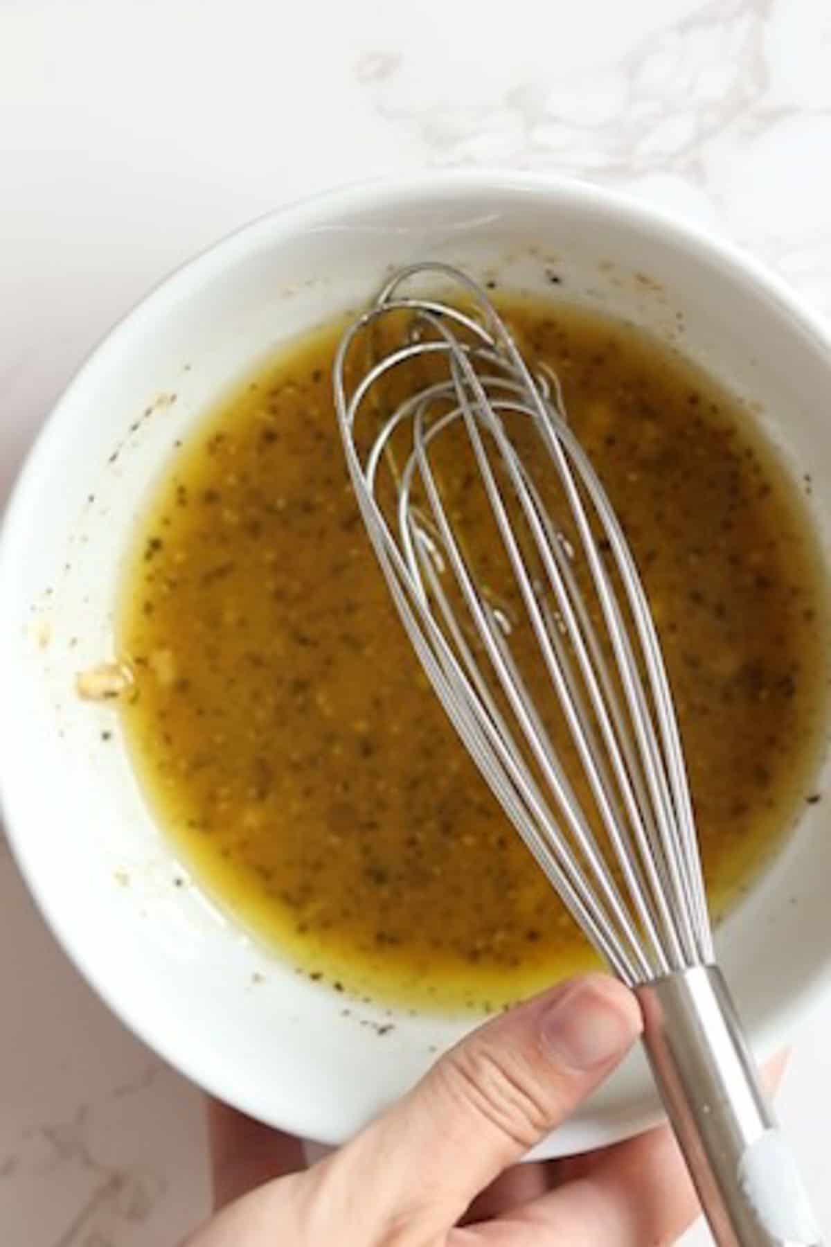 dressing in a white bowl with a whisk