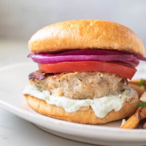 chicken burger on a white plate with tzatziki sauce, tomato, and red onion