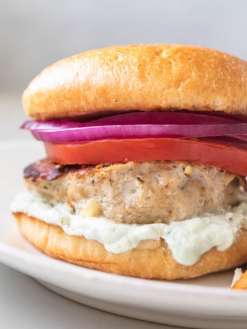 chicken burger on a white plate with tzatziki sauce, tomato, and red onion