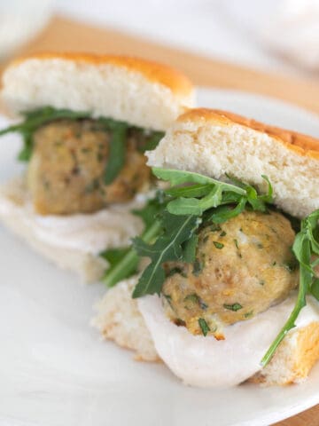 two chicken meatball sliders on a white plate with arugula and yogurt sauce