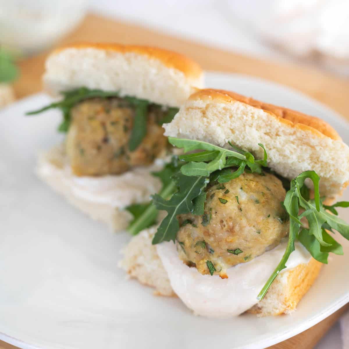 Two chicken meatball sliders on a white plate with arugula and yogurt sauce.