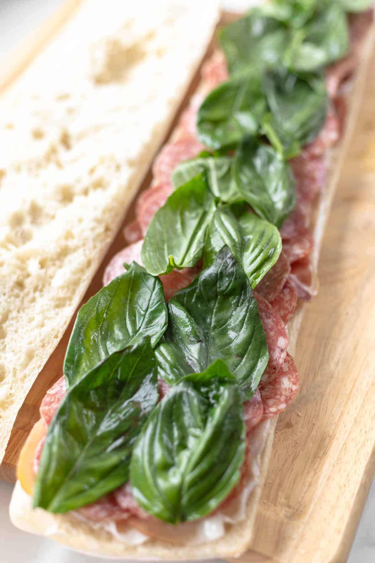 salami and basil layered on bread next to plain bread on a wooden cutting board