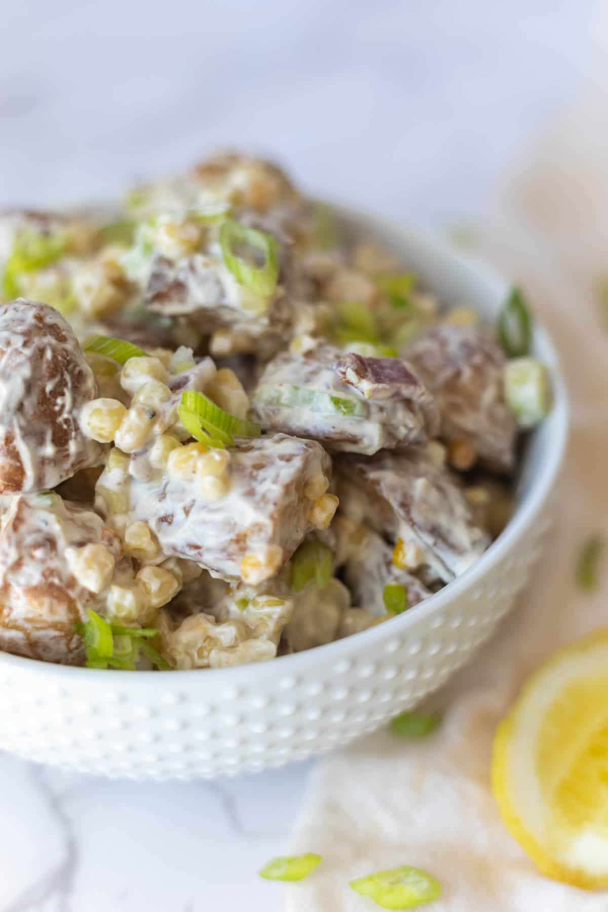 close up of roasted potato salad in a white bowl with a lemon wedge