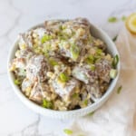 roasted potato salad in a white bowl topped with green onions on a white counter with a lemon wedge on the side