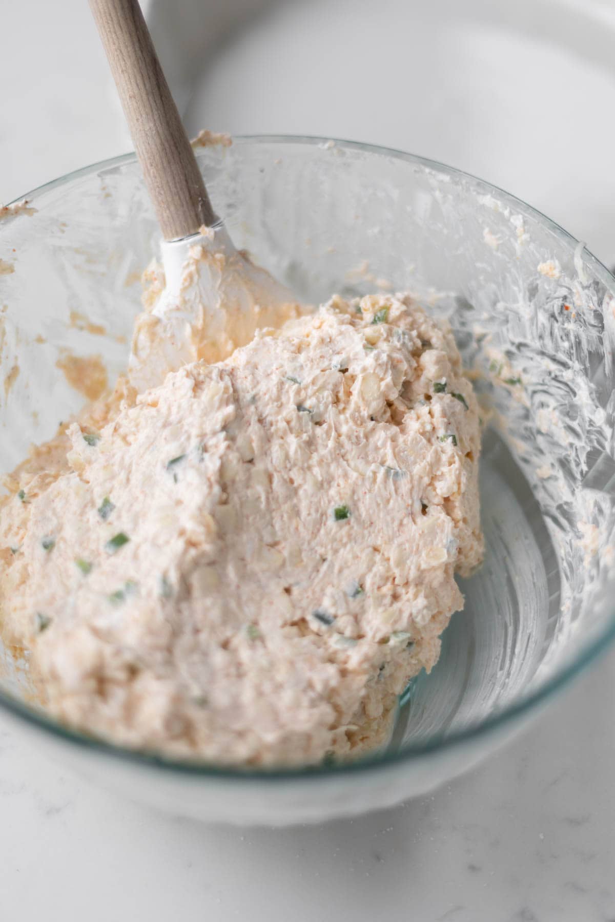 dip ingredients mixed together in a clear bowl with a wooden spoon