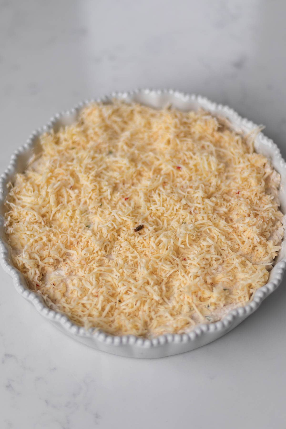 unbaked corn dip in a white tart pan topped with shredded pepperjack cheese
