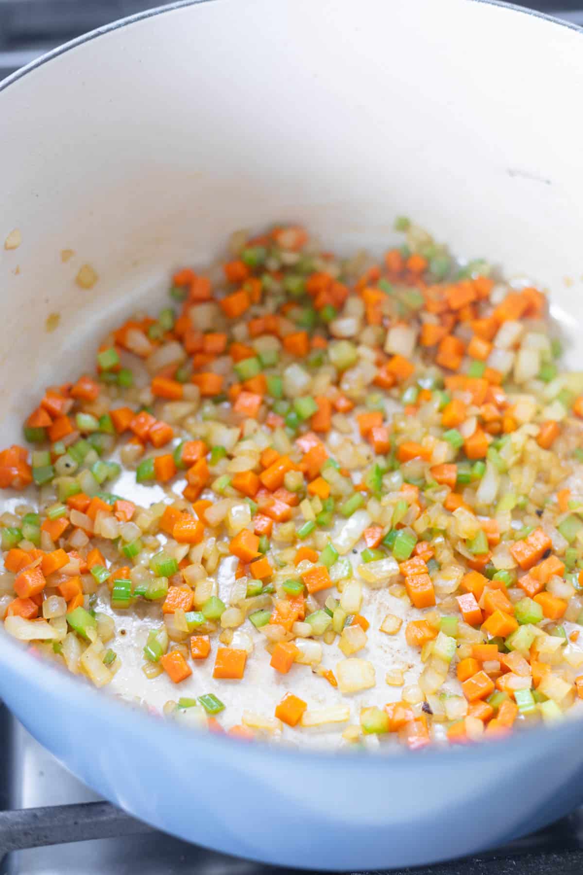 diced celery, carrots, and onions in a blue dutch oven cooking