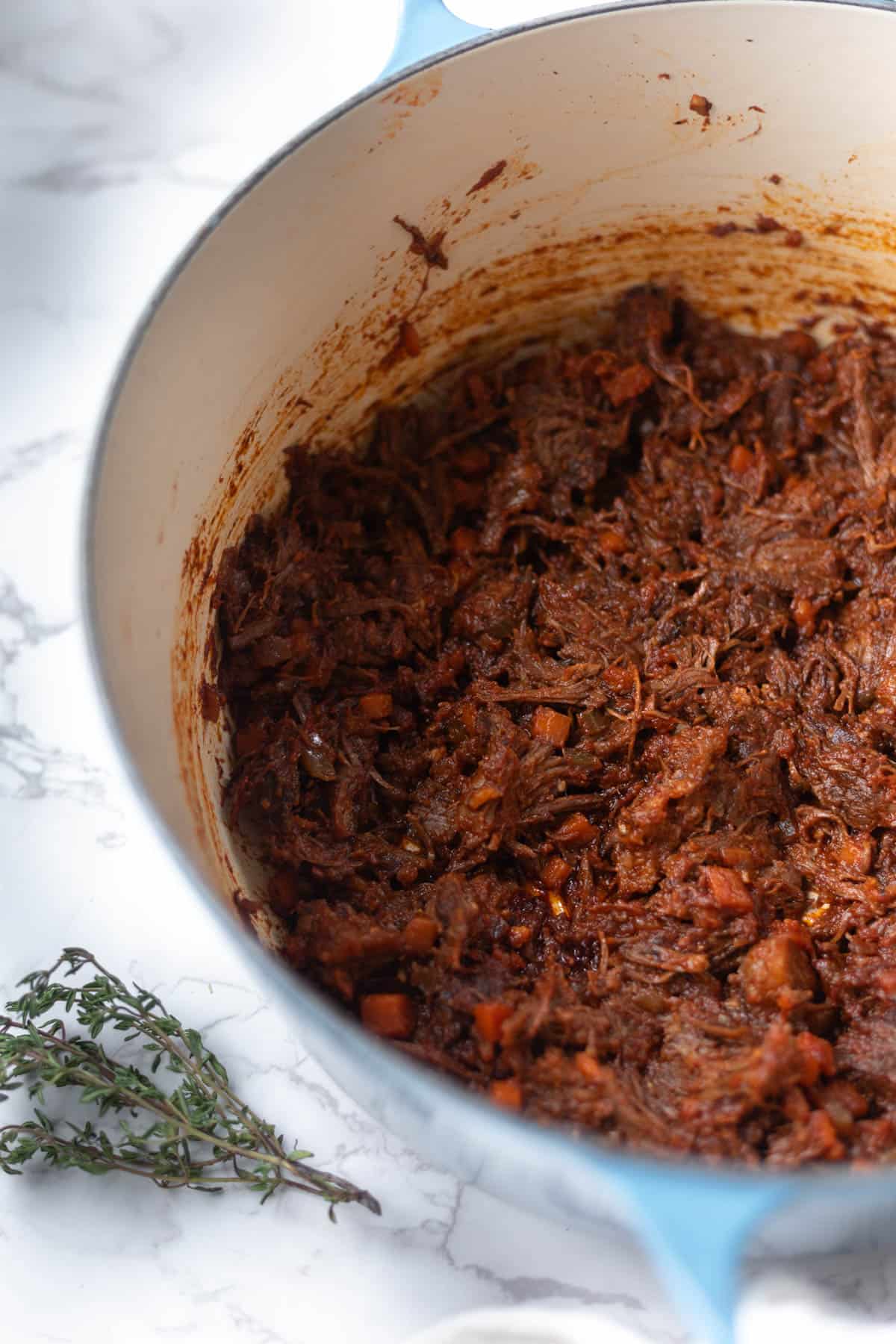 shredded short rib ragu in a dutch oven next to thyme