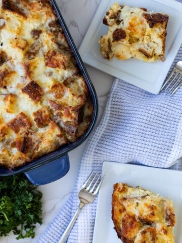 two white plates of breakfast strata next to the casserole of strata and parsley