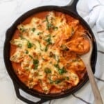 stuffed pasta shells in red sauce in a cast iron skillet being scooped by a wooden spoon