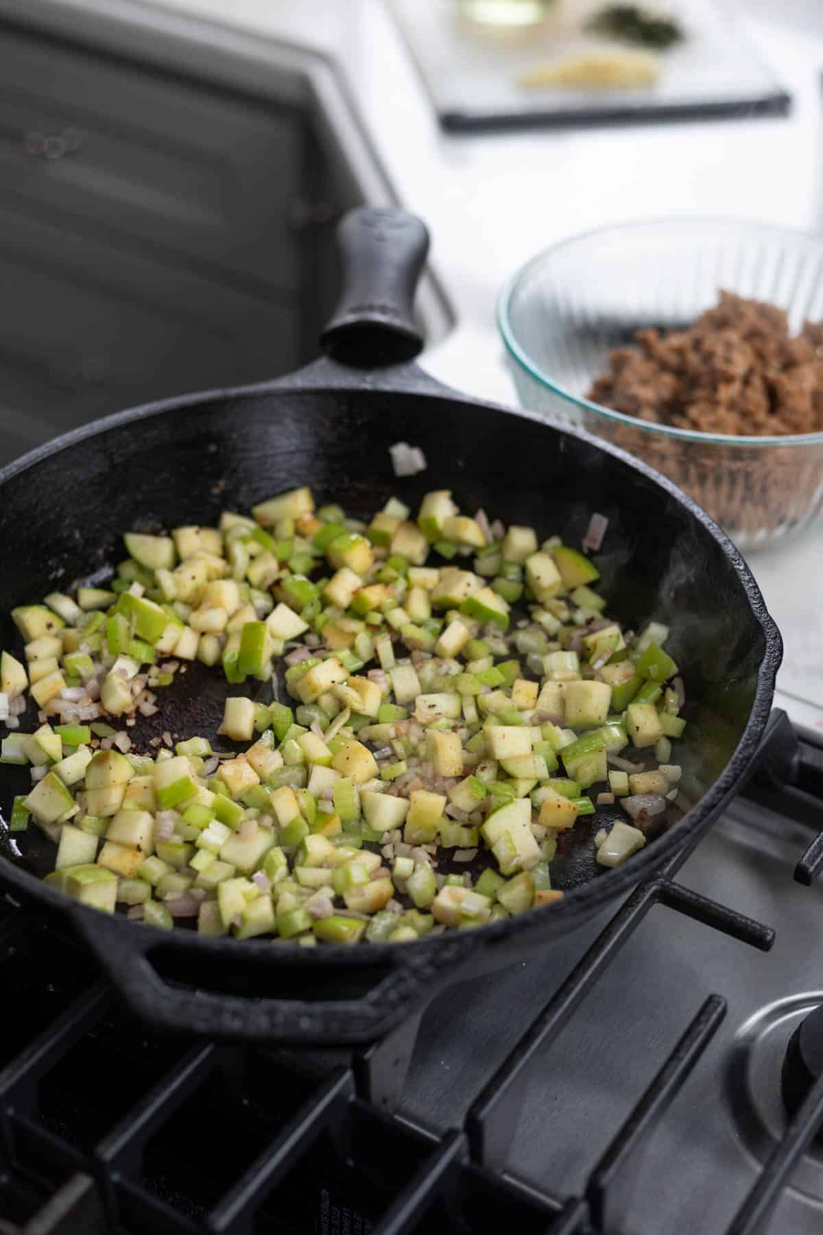 apples, celery, shallot, and herbs cooking in a cast iron skillet